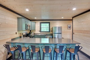 Una cocina con paredes de madera, una isla central con taburetes de bar, electrodomésticos de acero inoxidable y una ventana.