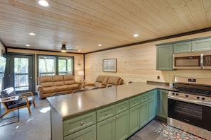 A kitchen with wooden ceiling, green cabinets, a stainless steel stove, and a dining area with a sofa and chairs.