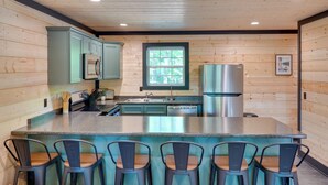 A kitchen with wooden walls, a central island with bar stools, stainless steel appliances, and a window.