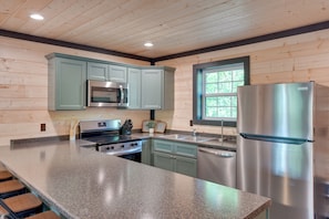 A kitchen with wooden walls, a granite countertop, stainless steel appliances, and a window.
