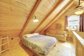 Una habitación de madera con cama, sofá, escalera y ventana.
