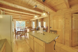 A wooden cabin interior with a kitchen island, dining table, chairs, and a refrigerator.