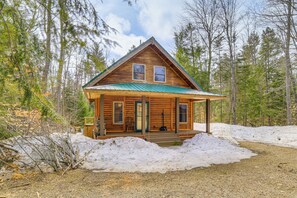 A log cabin with a porch, two windows, and a metal roof.