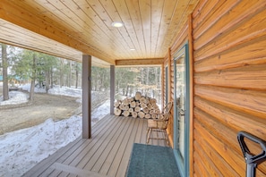 A wooden cabin with a porch, a chair, and a stack of logs.