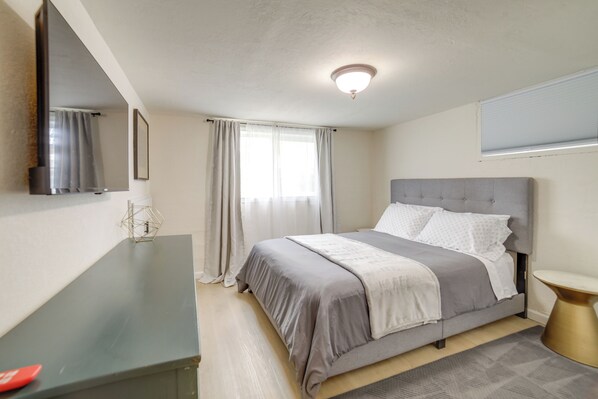 A bedroom with a bed, a desk, a mirror, and a window with curtains.