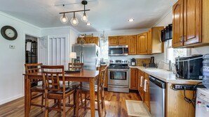 A kitchen with wooden cabinets, stainless steel appliances, a dining table with chairs, and a water dispenser. - Dog-friendly Waneta Lake Home w/ Lake Access! (Hammondsport)