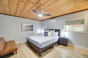 Un dormitorio con techo de madera, una cama con ropa de cama blanca, una mesita de noche, un sofá marrón y una ventana con persianas.