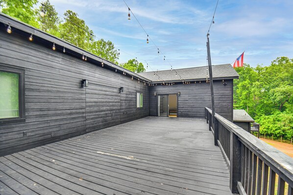 A wooden deck with string lights, a flag, and a building with a door.
