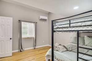 Une chambre avec un lit superposé, une fenêtre avec des stores, un appareil de climatisation et un plancher en bois.