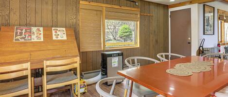 A wooden-paneled room with a table, chairs, a refrigerator, and a window with a view of trees.