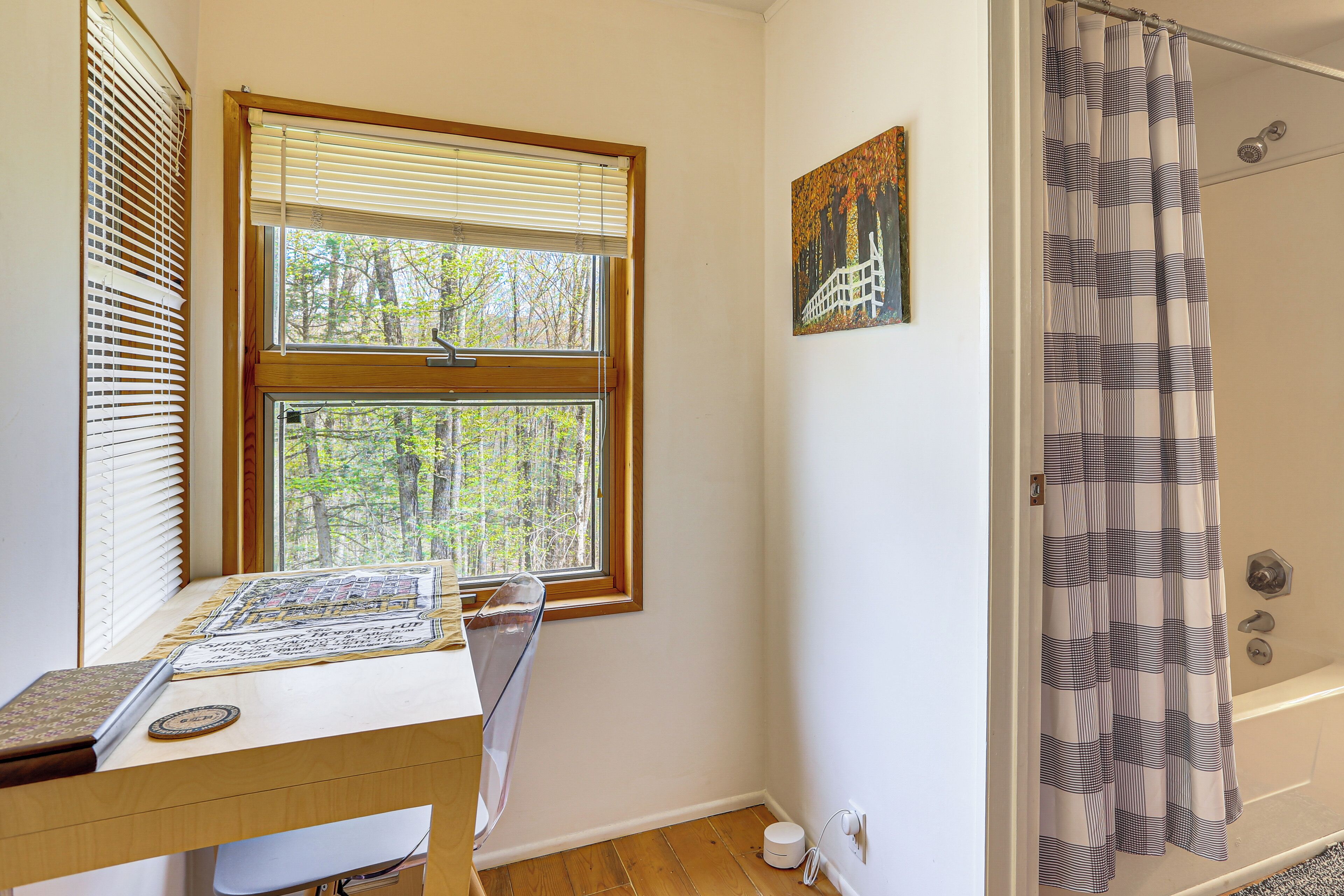 A bathroom with a shower curtain, a window with blinds, and a painting on the wall.