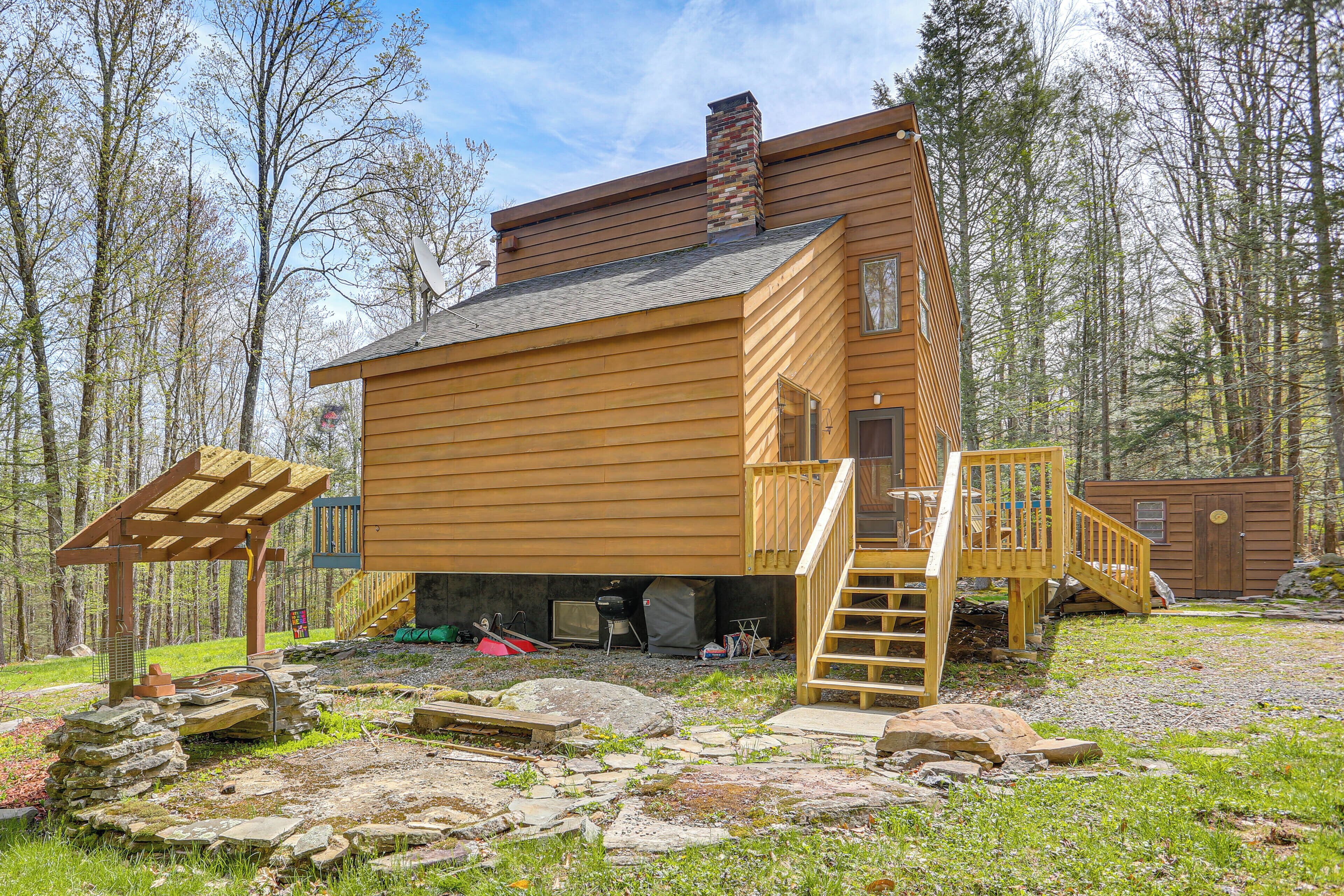 A wooden cabin with a wooden deck, a chimney, and a small attached shed.
