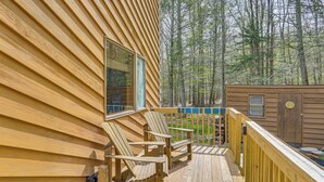 A wooden deck with Adirondack chairs, a small shed, and a forested backdrop. - Catskills Serenity! Cozy Vintage Cabin on 10 Acres (Grahamsville)