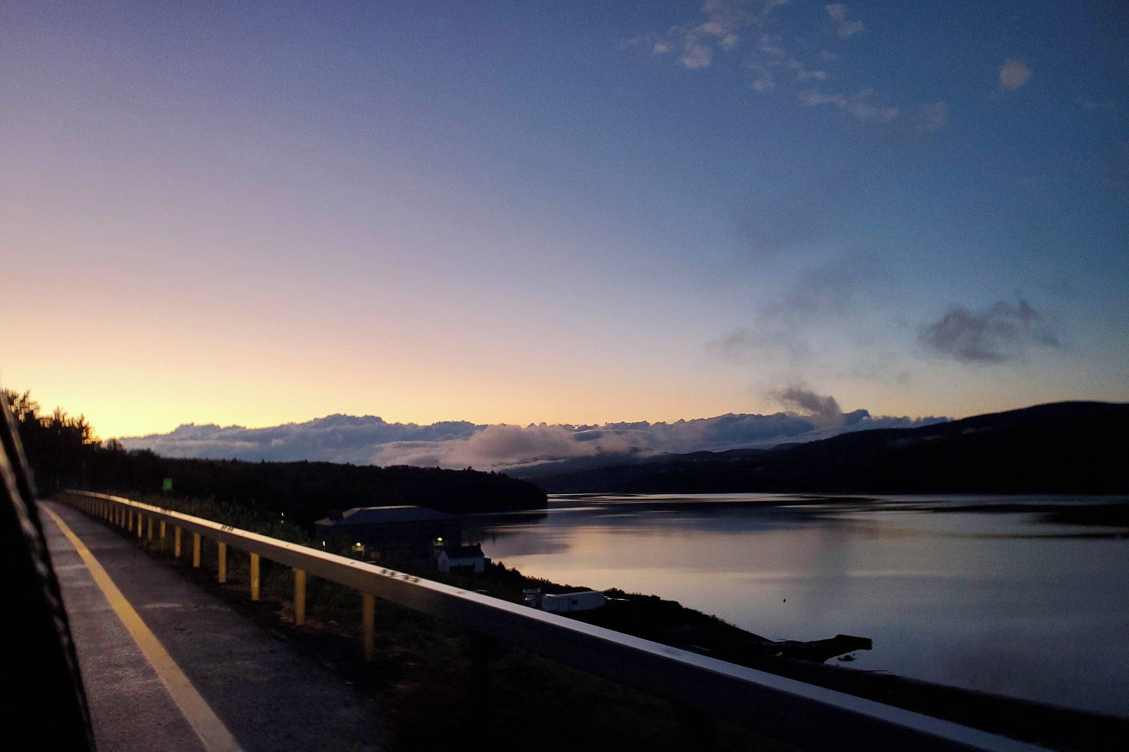 A bridge with a guardrail, a calm lake, and distant mountains.