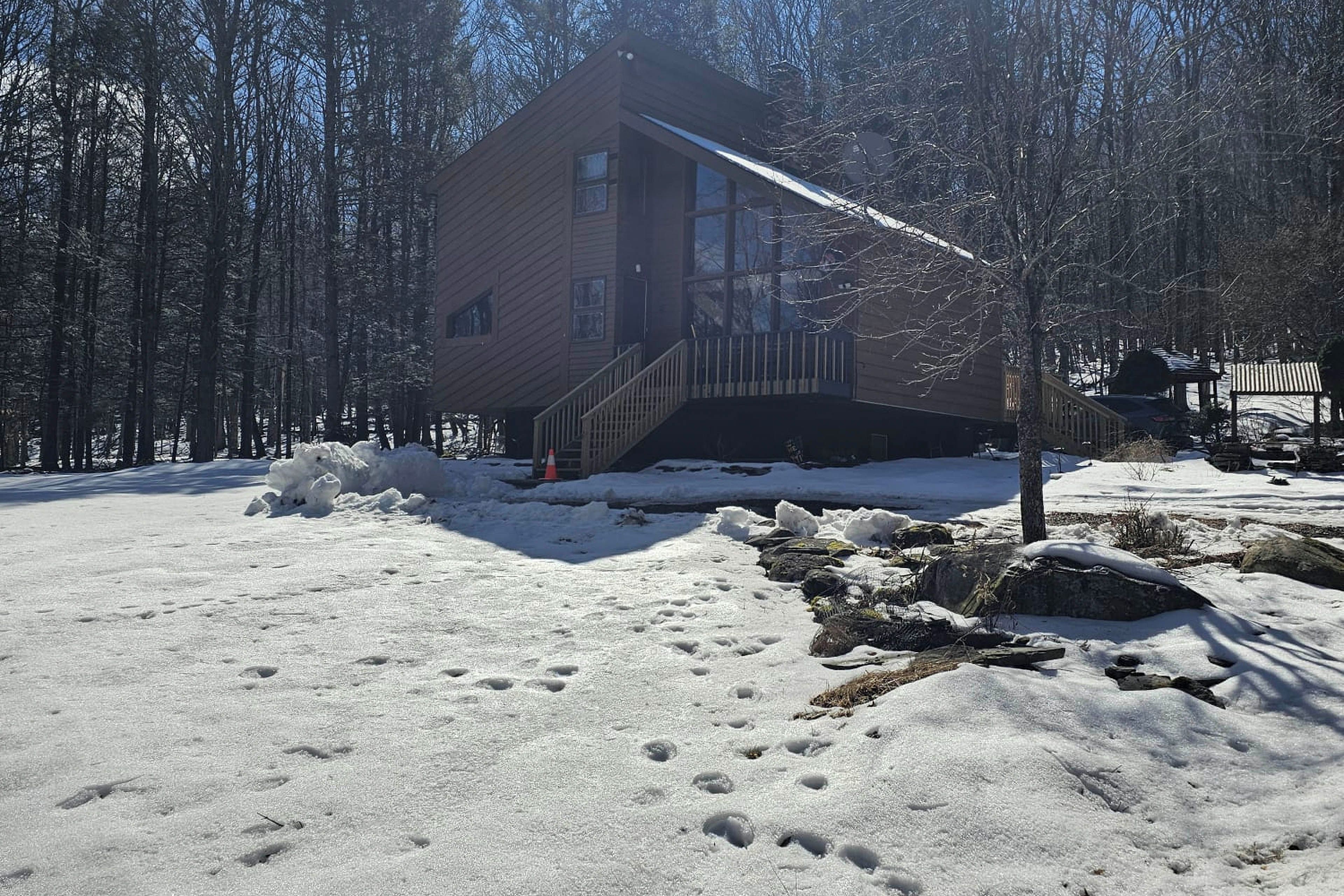 A cabin with a wooden exterior, a covered staircase, and a snow-covered ground with footprints.