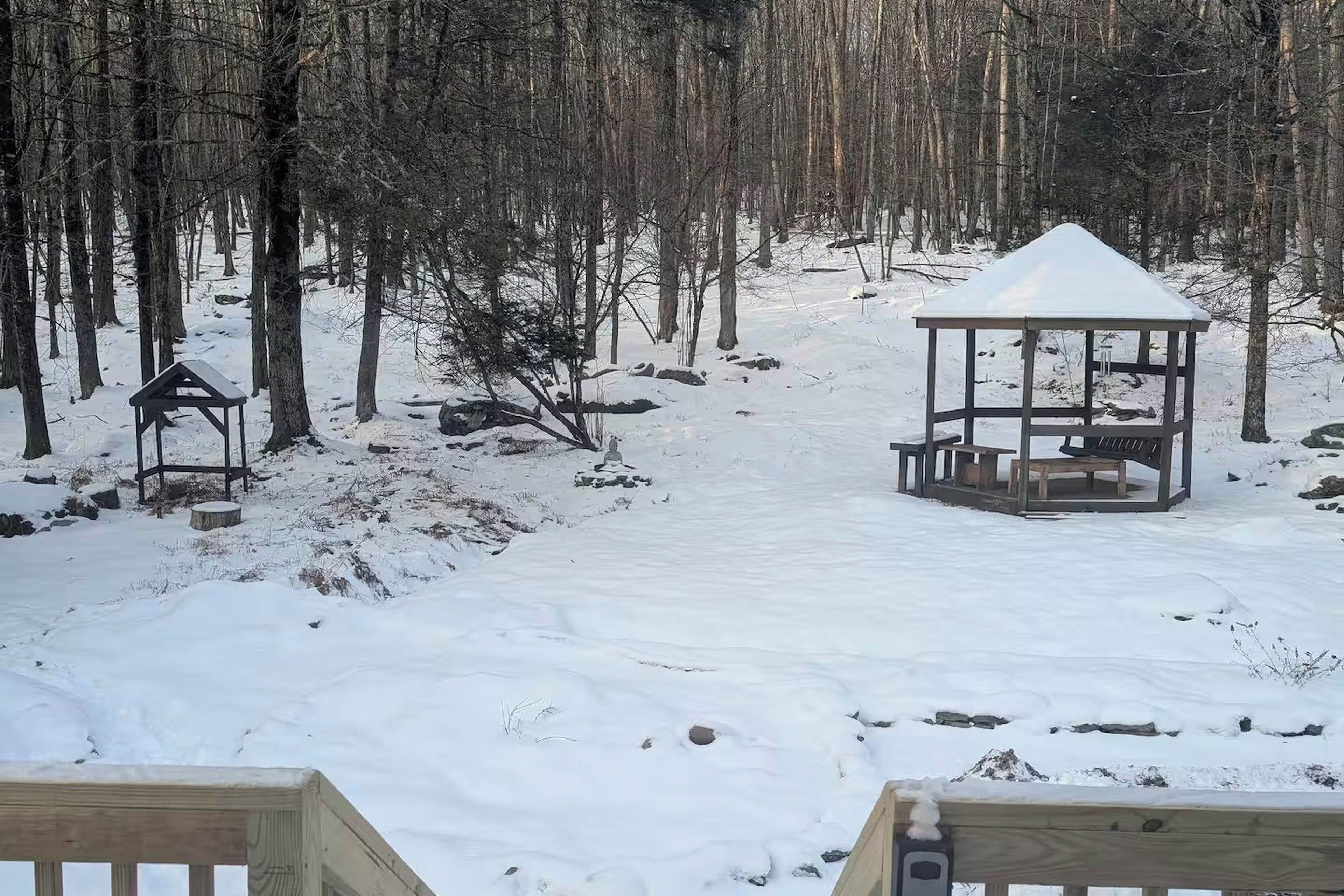 A snow-covered forest with a gazebo and a wooden bench.