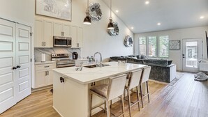 Una cocina amplia con una isla central, armarios blancos, electrodomésticos de acero inoxidable e iluminación colgante.
