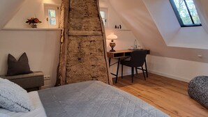 Un dormitorio tipo loft con techo inclinado, estructura de vigas de madera, cama con cubrecama acolchado, un escritorio y una silla.