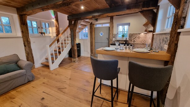 Un interior rústico con una escalera de madera, una zona de comedor con taburetes de bar y un sofá.