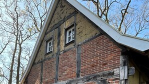Un edificio de ladrillo tradicional con una puerta verde, una mesa pequeña con mantel y una silla afuera.