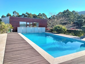 A modern pool area with a wooden deck, a rectangular pool, and a building with large windows. - Casa Santa Luzia (Âncora)