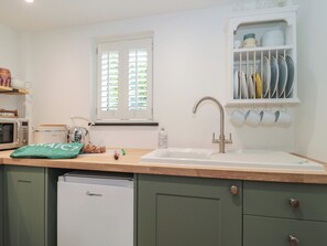 A kitchen with a dishwasher, a sink, a window with blinds, and a dish rack. - Rubys Den (Swindon)