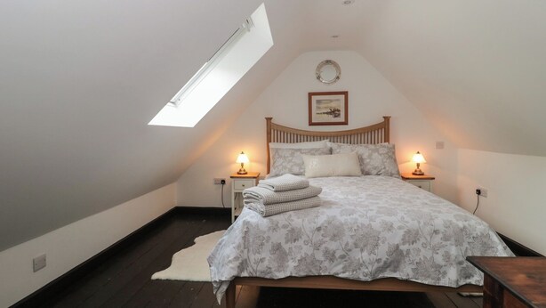 Quarto com clarabóia, cama com roupa de cama florida, duas mesas de cabeceira com abajures e um quadro na parede.