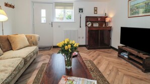 Uma sala de estar com sofá, mesa de centro com um vaso de flores, armário de madeira com rádio, televisão e um quadro na parede.