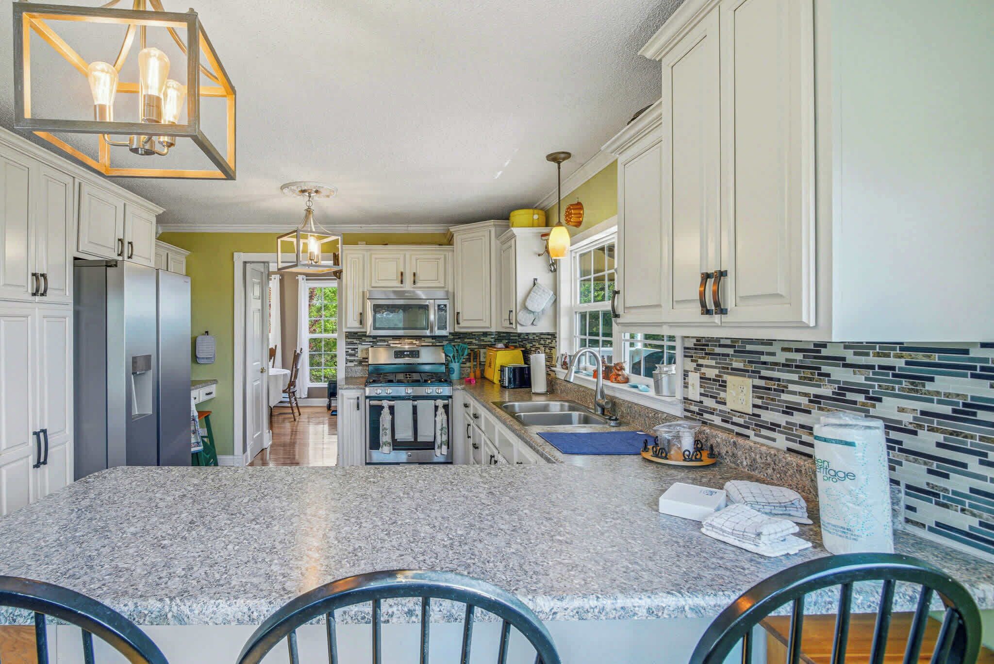 A kitchen with white cabinets, granite countertops, stainless steel appliances, and a hanging light fixture.
