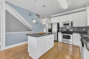 Eine moderne Küche mit weißen Schränken, einer Granit Arbeitsplatte, einem Einbauofen, einer Mikrowelle und einem Edelstahl-Kühlschrank.
