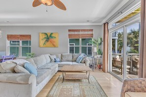 Ein geräumiges Wohnzimmer mit einer großen Eckcouch, einem kleinen Couchtisch und einem großen Fenster mit Jalousien.