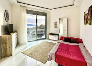 Ein modernes Schlafzimmer mit einer großen Schiebeglaswand, einem Flachbildfernseher, einem Bett mit roter Bettwäsche, einer hölzernen Kommode und einem weißen Kleiderschrank.