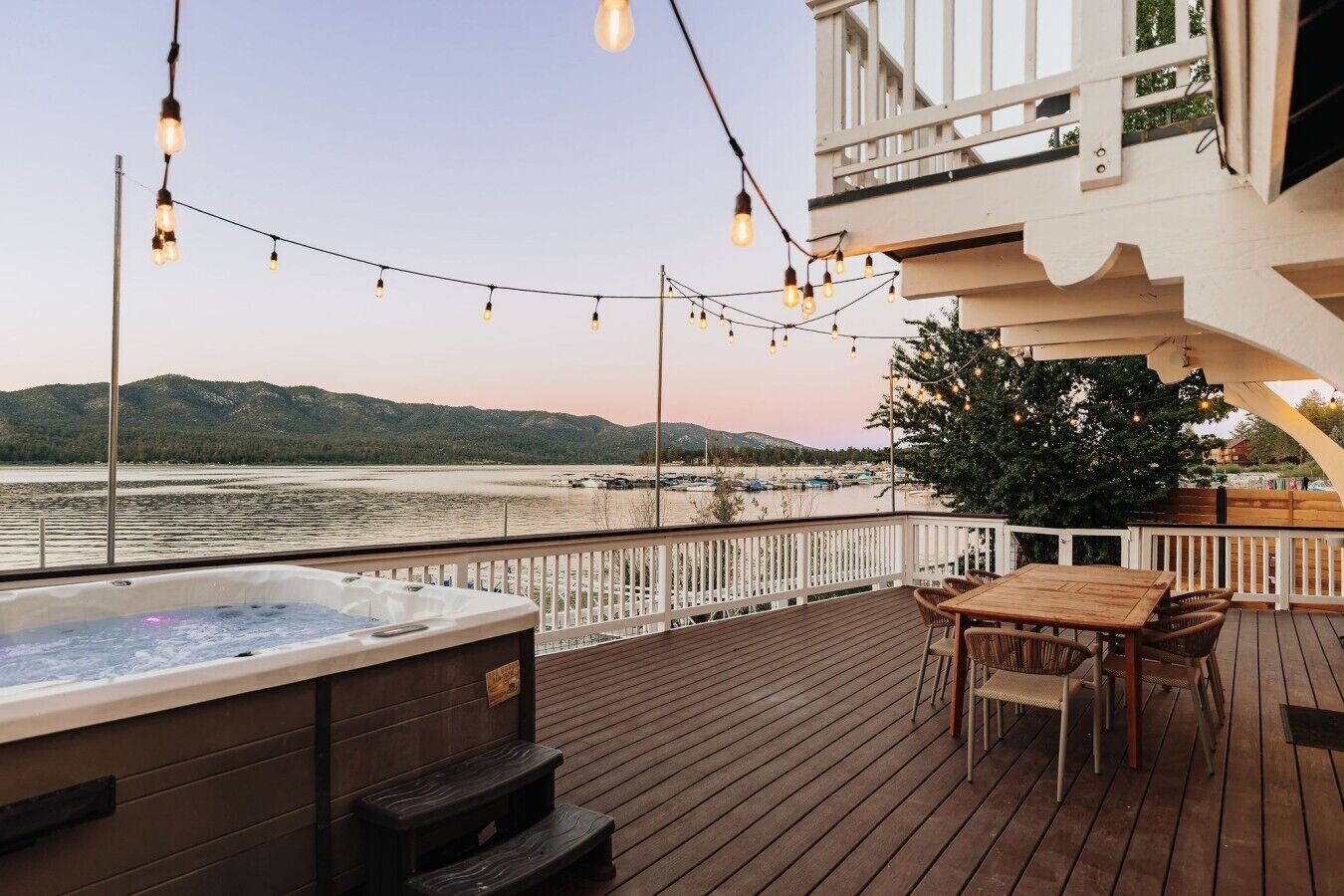 A wooden deck with a hot tub, outdoor seating, and string lights.