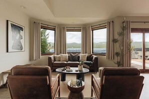 A living room with a sofa, chairs, a coffee table, and a view of a lake and mountains through large windows. - Lakefront Luxe Lodge w/Dock & Hot Tub near Village (Big Bear Lake)