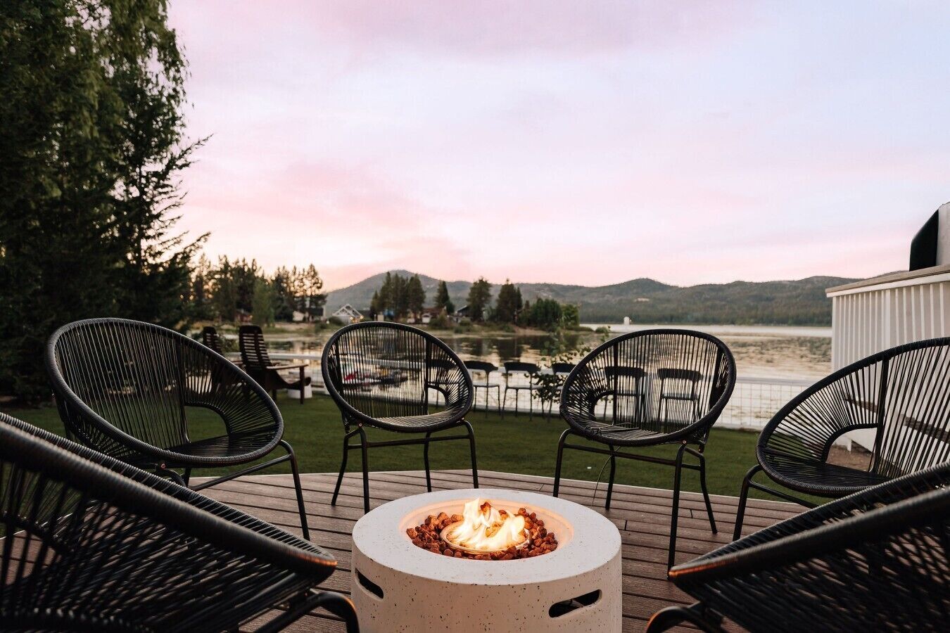 A deck with outdoor seating and a fire pit, overlooking a body of water and hills.