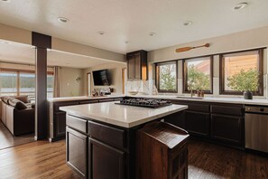 A modern kitchen with a large island, dark cabinetry, and a view of the outdoors. - Lakefront Luxe Lodge w/Dock & Hot Tub near Village (Big Bear Lake)