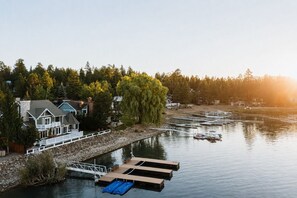 A waterfront property with a dock, a house with a porch, and a forested area. - Lakefront Luxe Lodge w/Dock & Hot Tub near Village (Big Bear Lake)