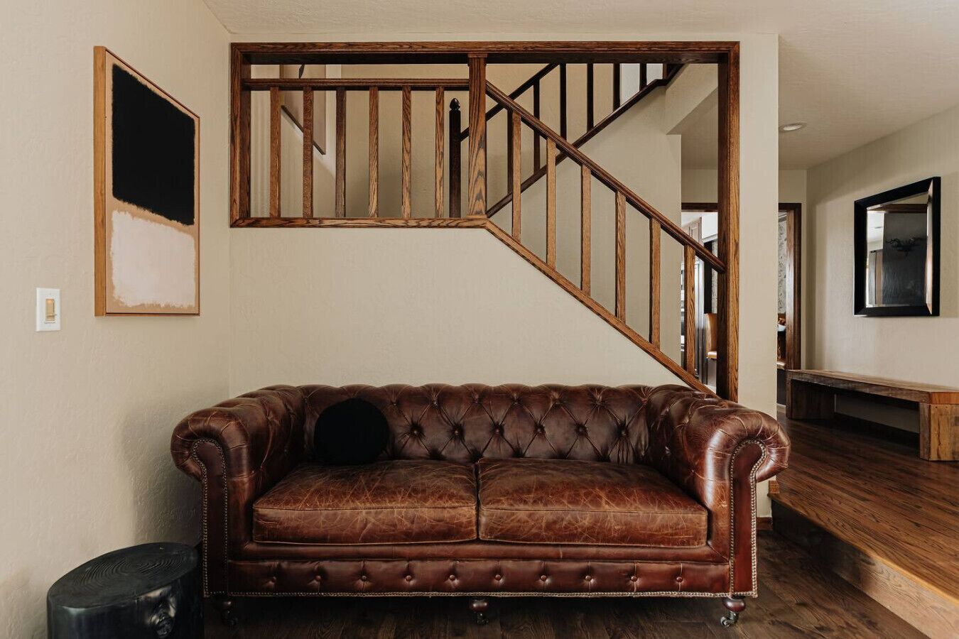 Un canapé en cuir marron avec un coussin noir, un escalier en bois et un tableau encadré au mur.