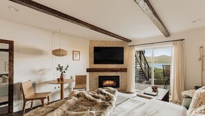 Een slaapkamer met een open haard, een televisie, een eethoek en uitzicht op een meer.