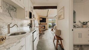 Een keuken met marmeren aanrechtbladen, een spoelbak en kasten. Er is een eethoek met een tafel en stoelen, en een open haard.