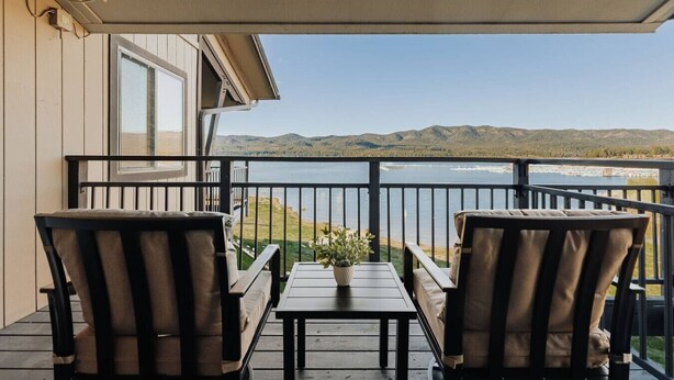 Een balkon met twee stoelen en een tafel, met uitzicht op een meer en bergen.