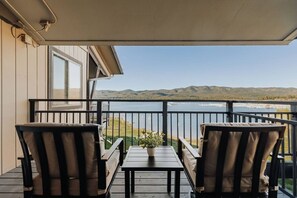 A balcony with two chairs and a table, overlooking a lake and mountains.