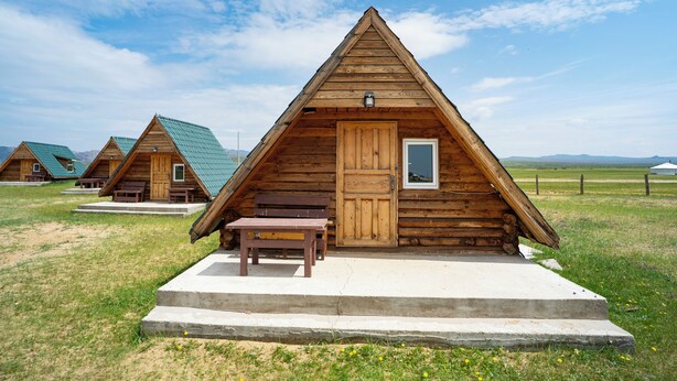 A wooden cabin with a pitched roof, a door, and a window.