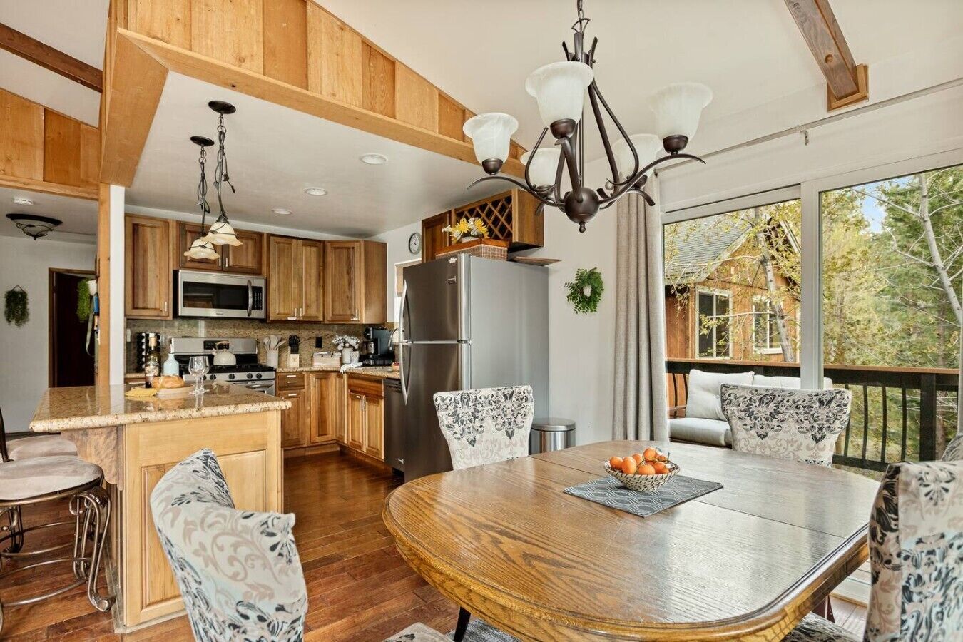 A modern kitchen with wooden cabinets, stainless steel appliances, and a dining area with a round wooden table and patterned chairs.