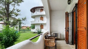 Uma varanda com mesa e cadeiras, vista de um edifício com várias varandas e uma árvore.