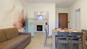 Cozinha moderna com forno embutido, mesa de jantar com cadeiras e um sofá numa sala de estar.
