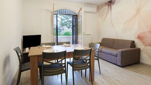 Uma sala de jantar com mesa de madeira, cadeiras pretas, um sofá marrom e uma televisão à esquerda.