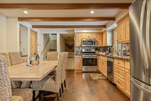 Una cocina con armarios de madera, electrodomésticos de acero inoxidable y un comedor con mesa de madera y sillas de fibras naturales.