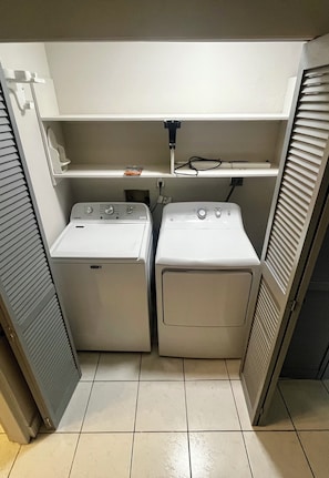 A laundry room with two white front-loading washing machines, a shelf above, and a power outlet. - Serene, Picturesque,Secluded!!Nestled atop a mountain looking at the ocean (St Thomas)