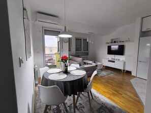 En kompakt opholdsstue med spiseplads, tekøkken og TV.